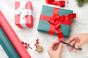 Woman making Christmas gift on light background