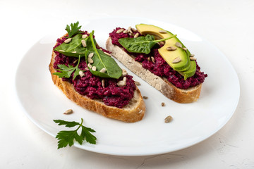 Wall Mural - Bruschettas with beetroot hummus, avocado, spinach and seeds on a white plate on a white background.