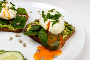 Wall Mural - Poached eggs with avocado, spinach leaves and seeds on toasts bread on a white plate on the white background. Healthy breakfast or snack.