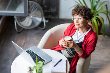 Wall Mural - young female designer with cup of coffee sitting in armchair in cafe