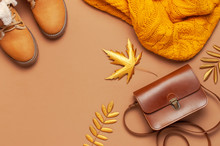 Brown Leather Women Bag, Orange Knitted Sweater, Warm Boots, Golden Autumn Leaf On Brown Background Top View Flat Lay. Fashionable Women's Accessories. Autumn Fashion Concept. Stylish Lady Clothes