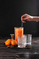 Fresh tangerines with cinnamon in a decanter on a dark background next to two glasses