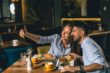 happy young couple taking picture while eating in cafeteria