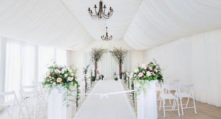 Indoor wedding ceremony with white wedding arch decorated with flowers and big white candles