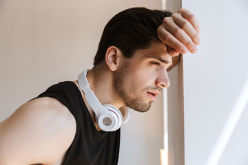 Wall Mural - Handsome young sports man standing near window with headphones on neck.