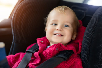 Cute caucasian toodler boy sitting in child safety seat in car during road trip. Adorable baby smiling and enjoying trip in comfortable place in vehicle. Children care and safety on road