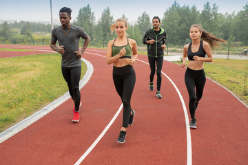 Poster - Group of active guys and girls in sportswear running down racetracks on stadium