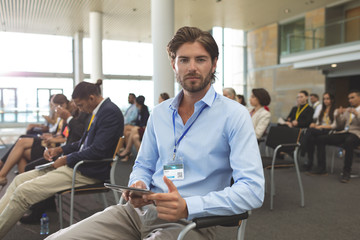 Wall Mural - Young businessman with digital tablet looking at camera during seminar