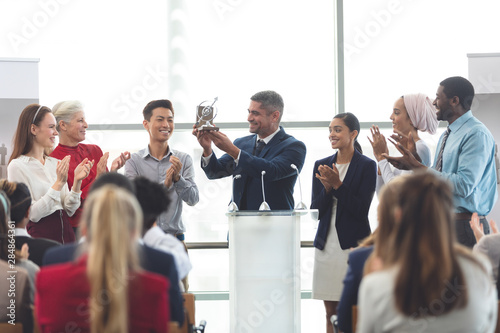 Cuadros en Lienzo Businessman holding award at podium with colleagues in a business seminar