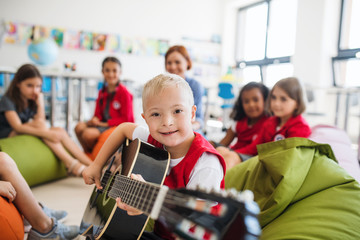 Wall Mural - A down-syndrome boy with school kids and teacher sitting in class, playing guitar.