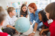 © Halfpoint - A group of small school kids with teacher sitting on the floor in class, learning.
