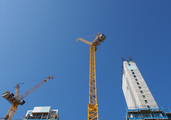 Wall Mural - a view of tall tower cranes working on large construction sites against a blue sky in leeds england