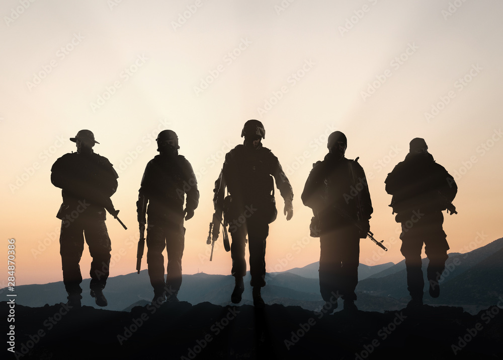 Military silhouettes of soldiers against the backdrop of sunset sky. - obrazy, fototapety, plakaty 