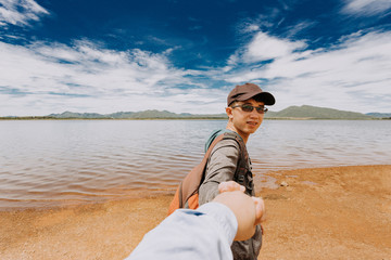 Asian male backpacker holding his girlfriend to go traveling at reservoir on beautiful blue sky