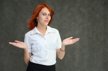 Photo Portrait of a cute girl woman with bright red hair manager in a white shirt on a gray background in the studio. He talks, shows his hands in front of the camera with emotions.