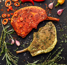 Raw bone-in pork chops, tomahawk steak marinated in aromatic marinades with fresh herbs and spices on a dark background, top view