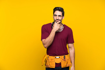 Handsome young craftsman over isolated yellow background thinking an idea