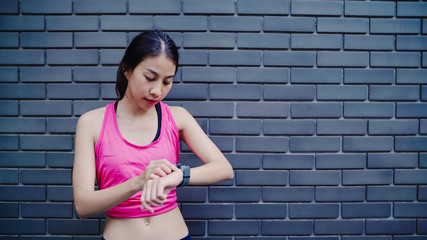 Healthy beautiful young Asian Athlete woman setting and checking progress looking heart rate monitor on smart watch while running in urban city. Lifestyle women exercise in the city concept.