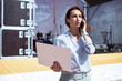 © Anton Gepolov - Installation of stage equipment and preparing for a live concert open air. Event manager portrait. Summer music city festival. Young serious woman stand and work with her laptop near the stage.