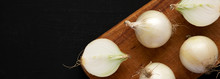 Raw White Onions On A Rustic Board On A Black Background, Overhead View. Flat Lay, Top View, From Above. Space For Text.