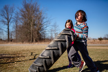 Two Small Children Work Together To Lift A Heavy Tire In A Park