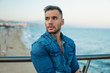 © Igor Kardasov - A young handsome man on the bridge near beautiful beach. Rich and successful male model wearing denim shirt