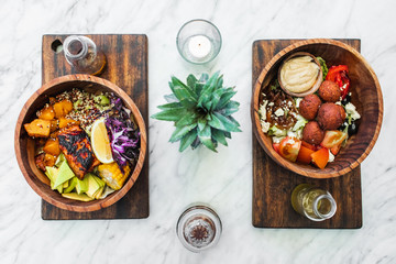 Flat lay of wooden bowls with fresh organic vegetarian food on white marble table. Falafel, hummus, avocado, vegetable salad, salmon steak. Olive oil on side. Healthy food concept.