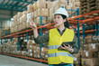 © PR Image Factory - warehouse worker woman in safety vests holding digital tablet and pointing up with finger. young girl staff wearing hard hat working in stockroom. elegant lady employee taking inventory in storehouse
