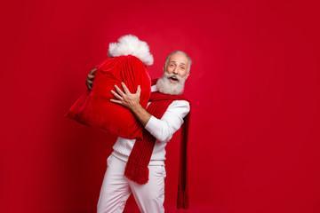 Hipster grey haired man unusual santa with traditionally large bag wear fashion knitted clothes isolated red background