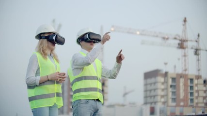 Two people in virtual reality glasses on the background of buildings under construction with cranes imitate the work of the interface for the control and management of construction