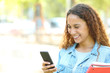 © Antonioguillem - Happy mixed race student checking phone in a park