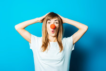 Beautiful Young Woman In A White T-shirt And Red Nose Of A Clown With A Surprised Face On A Blue Background. Concept Party, Costume, Red Nose Day
