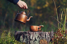 A Man Pours Coffee From A Vintage Kettle Into A Wooden Mug In The Autumn Forest.