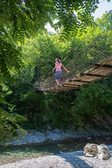  The girl walks along a suspended bridge among the forest above the mountain river. Bottom View