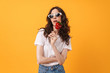 Young woman posing isolated over yellow wall background holding candy lollipop.