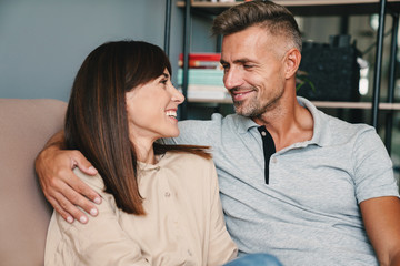 Wall Mural - Photo of middle-aged caucasian couple smiling while cuddling on sofa at home