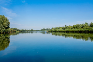 Blue beautiful sky against the background of the river. Clouds are displayed in calm water. On the horizon, the green bank of the Dniester, place for fishing