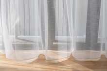White Transparent Curtain Above Wooden Floor At Glass Window.
