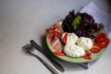 Poached egg - with slices of chili pepper, a sprig of dill, cherry tomatoes, Lettuce leaves and slices of bacon. For a healthy breakfast or snack. The plate lies on a gray napkin. Gray, stone backgrou