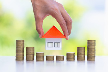 Woman hand hold a  home model put on the stack coin with growing, Savings money for buy house and loan to business investment for real estate concept.