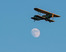 Green Antique Bi Plane With Yellow Trim Flying Past Full Moon