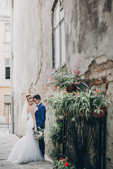 Wall Mural - Stylish happy bride and groom posing in old european city street. Gorgeous wedding couple of newlyweds embracing  outdoors. Romantic moment