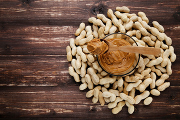 Peanut butter in bowl and spoon with nuts on brown wooden table