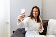 © pucko_ns - In bathrobe with coffee on hand woman use mobile phone and sitting on sofa in room