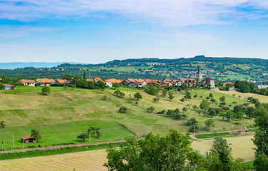 Hilly and picturesque landscape view of meadows, pastures, fields, trees, town of Brens and white clouds in the blue sky.Department of Haute-Savoie,region of Auvergne-Rhone-Alpes in France.