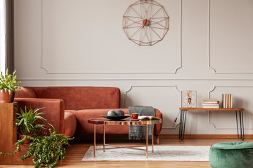 Brown comfortable corner sofa in elegant living room interior with grey wall with molding and fancy clock