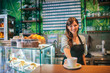 © bnenin - Portrait of a female barista standing behind the bar, serving coffee.