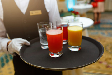 Waiter serving refreshing drinks. Glasses with water, orange juice, and berry juice on a tray. Waitor in black uniform at event party