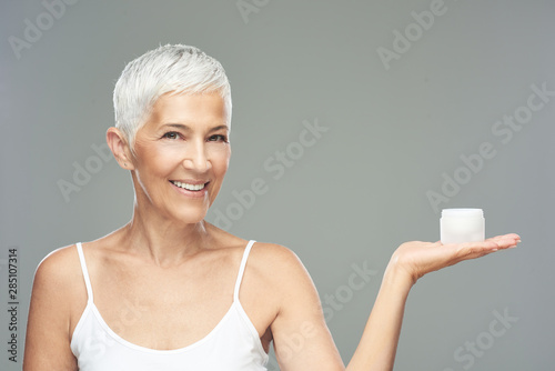 Fotomural Gorgeous smiling Caucasian senior woman trying out new anti age cream and looking at camera