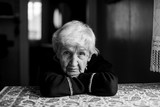 Fototapeta  - Elderly woman sitting in a dark room, black and white portrait.